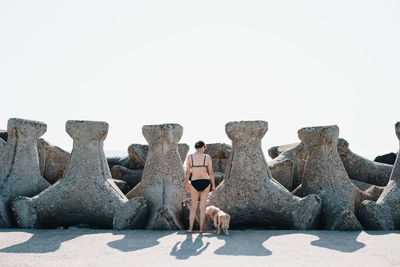 Rear view of woman standing by tetrapod rocks against clear sky