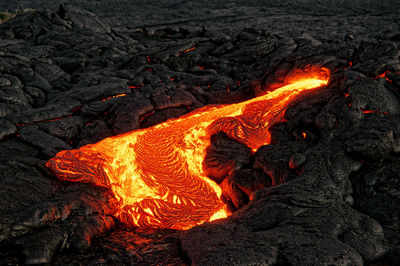 A lava flow emerges from a rock column and pours into a black volcanic landscape