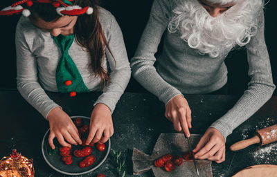 Two girls in santa claus hat with a beard and a headband  preparing pizza with ingredients .