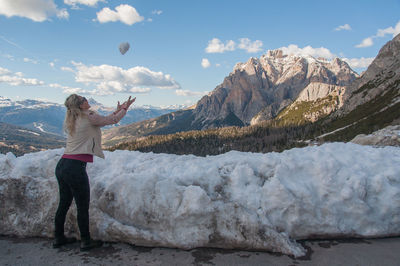 Side view of woman playing with snow on snowcapped mountains against sky