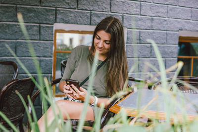 Smiling young woman using mobile phone while sitting outdoors