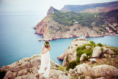 Portrait of a young woman with long hair in a white dress and a wreath on the rock, the mountain