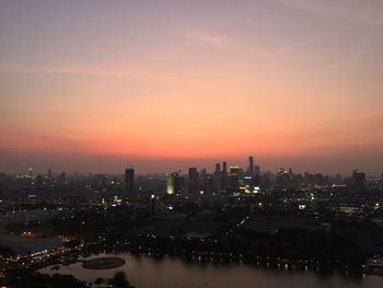 River by illuminated cityscape against sky during sunset