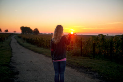 Woman standing on road against sky during sunset