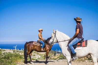 Friends riding horses at beach against sky