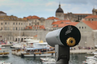Close-up of coin-operated binoculars against river and buildings in city