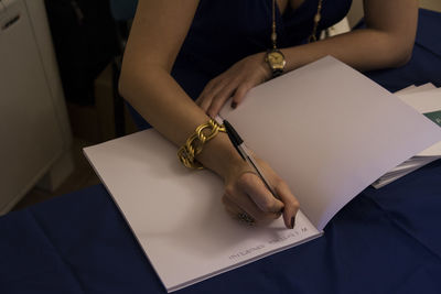 Midsection of woman holding paper while sitting on table