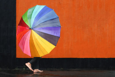 Low section of woman carrying colorful umbrella against wall