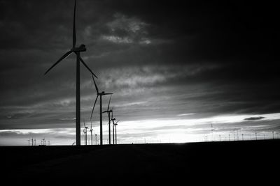 Silhouette windmills on field against cloudy sky