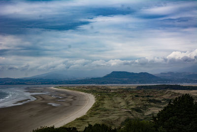 Scenic view of beach by mountains against cloudy sky