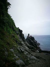 People on cliff by sea against sky