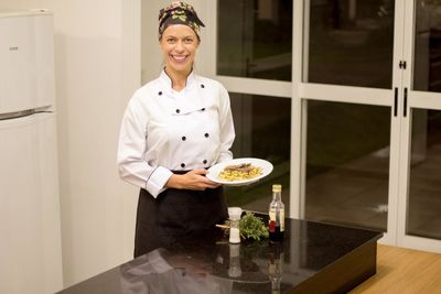 Portrait of happy female chef holding food in plate while standing in commercial kitchen