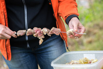 Midsection of man putting meat on skewer at back yard