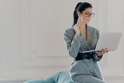 Businesswoman using laptop against wall