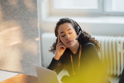 Young customer service representative wearing headset sitting with eyes closed in office