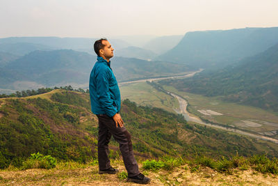 Man standing alone at hill top with misty mountain rage background from flat angle