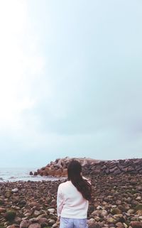 Rear view of woman standing on rock against sky