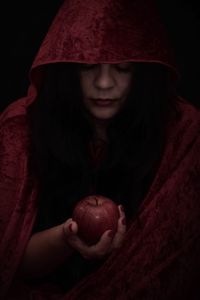 Portrait of a teenage girl holding apple against black background