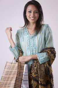 Portrait of smiling woman with shopping bags standing against gray background