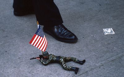 Low section of man walking by figurine and flag and paper currency on footpath in city