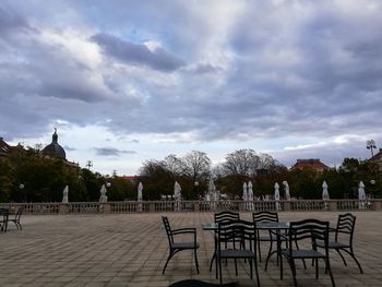 Empty benches in city against cloudy sky