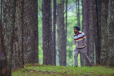 Man standing by tree trunk in forest