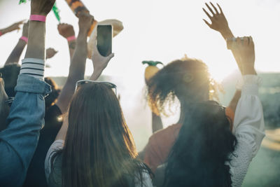 Woman holding smart phone while enjoying with friends at music festival