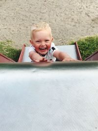 High angle portrait of happy boy sliding down slide at playground