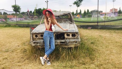 Full length of young woman standing by broken car on land