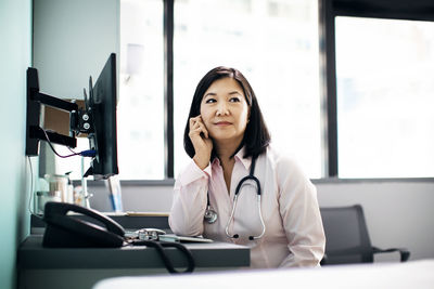 Thoughtful female doctor sitting at computer desk in clinic