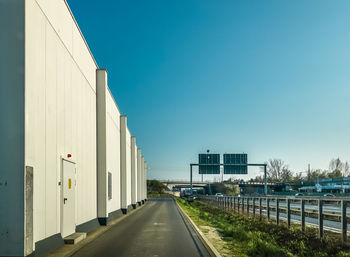 Road amidst buildings against clear blue sky