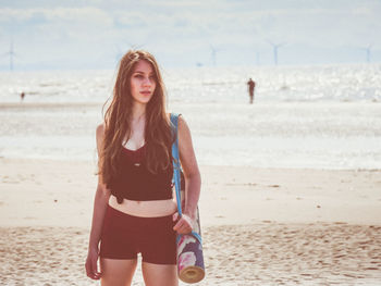 Young woman looking away while standing on sand at beach during sunny day