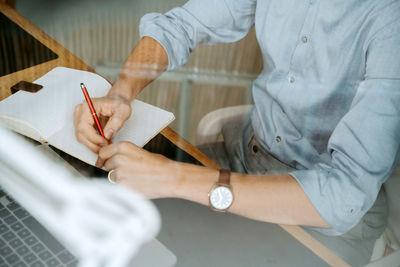 Unrecognizable crop male entrepreneur sitting at table and writing in notebook while planning business project