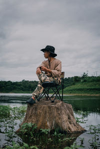 Man holding umbrella by lake against sky