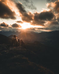 People sitting on rock against sky during sunset