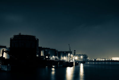 Illuminated factory by sea against sky at night