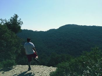 Rear view of man standing on mountain against clear sky