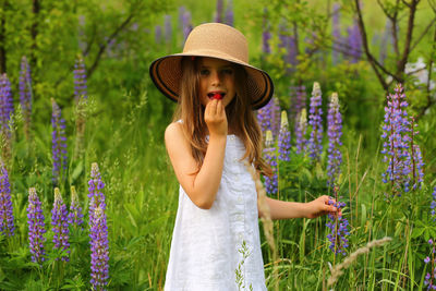 Portrait of a cute 6 year old girl eating strawberry in the delphinium field