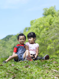 Portrait of siblings sitting on grassy field against trees