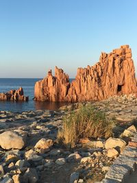 Rock formations by sea against clear blue sky