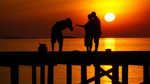 Silhouette men standing by sea against orange sky