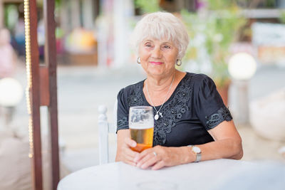 Mature woman sitting at a table in a summer cafe and drinking beer