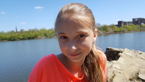 Portrait of teenage girl on rock formation by lake against sky