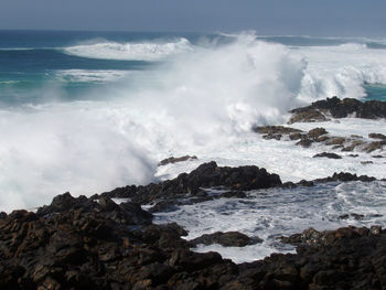 Waves breaking on rocks at shore against sky