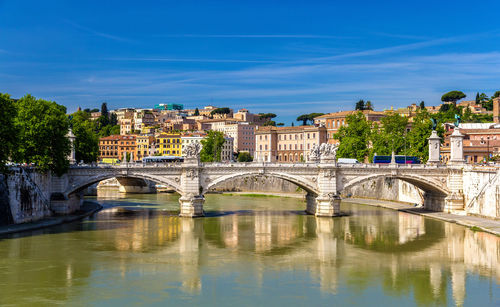 Bridge over river by buildings against blue sky