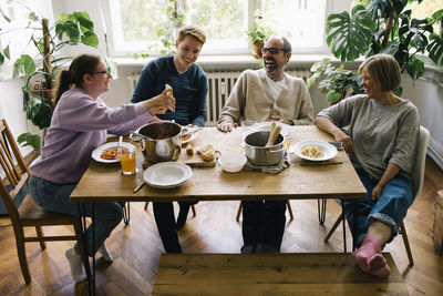 Happy family enjoying while sharing smart phones sitting at dining table in home