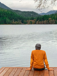 Rear view of man sitting by lake against mountain