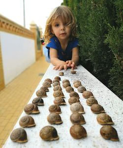 Portrait of cute girl lying by snails on retaining wall