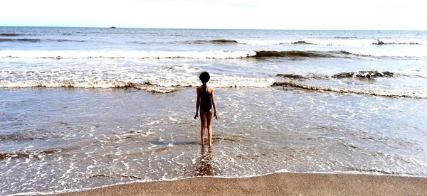 Rear view of man standing on beach against sky