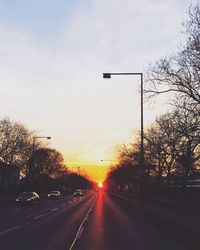 Road by trees against sky during sunset